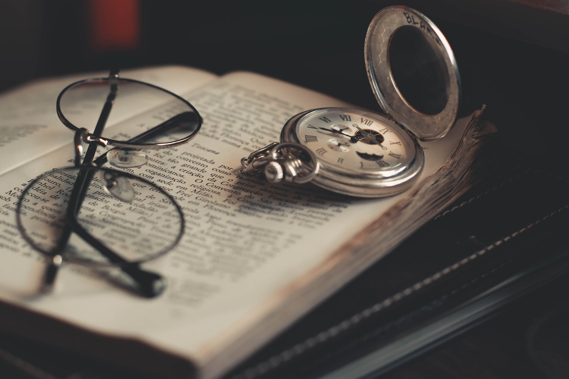 round silver colored pocket watch and eyeglasses on opened book