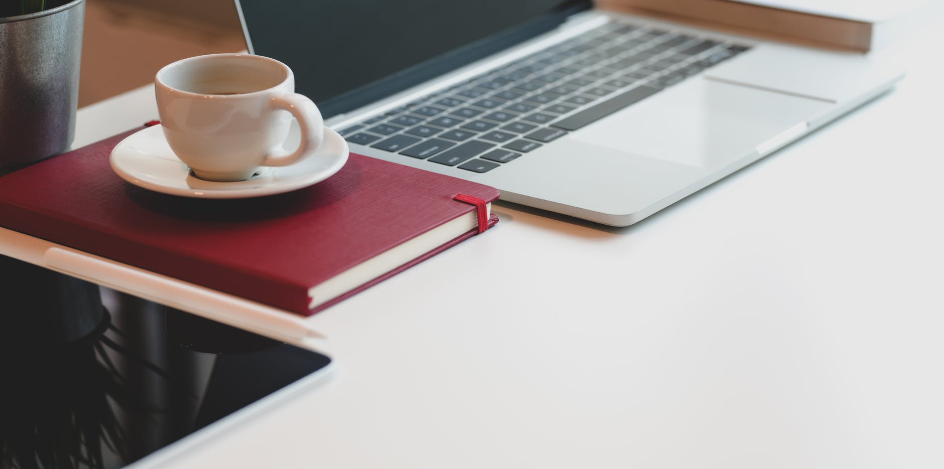white ceramic cup on white saucer beside macbook pro