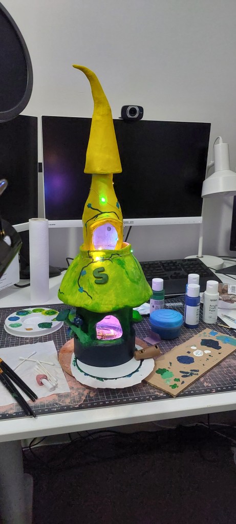 Fairy house music box, painted in greens and yellows with fairy lights in the jar and bottle.
