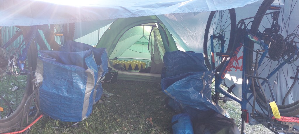 Shows two bicycles unpside down to prop up a tarp connected to the entrace of a tent, proving an extended shelter.